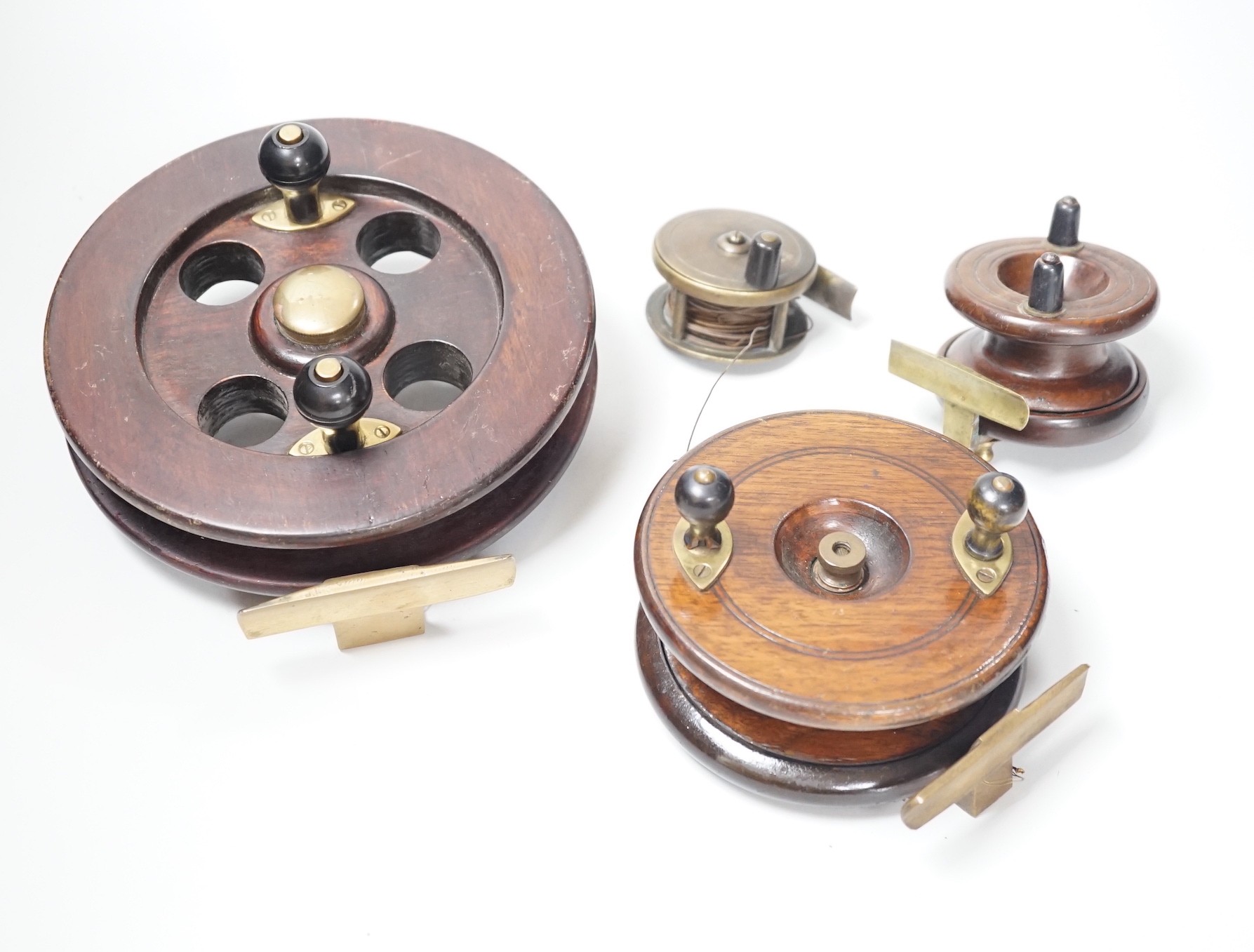 Three mahogany and brass fishing reels, largest 19 cm diameter and an Army & Navy brass reel, 6.3cm diameter